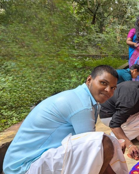 Students at AIAT create colorful rangoli designs on the ground outside a campus building surrounded by greenery. They are smiling and working together, dressed in traditional attire. The left side of the image has the AIAT logo and text that reads: 'YOU + US = YOUTH EMPOWERED. With your donations, we can help our students find their calling.
